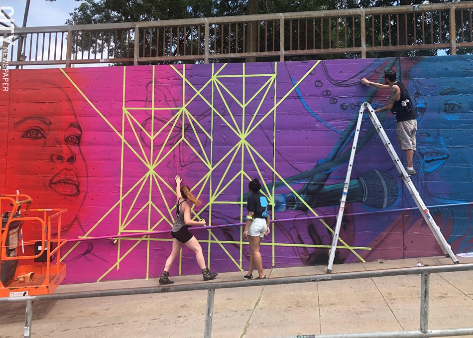 Artist Sarah Rutherford and youth apprentice Tehya Bollar tape off geometric lines while artist Justin Suarez (aka Mr. Prvrt) applies paint to "This is Triumphant Music," the Wall\Therapy mural featuring Rochester musicians at Martin Luther King Jr. Park. - PHOTO BY REBECCA RAFFERTY