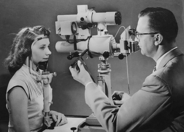 Bausch + Lomb has deep innovation history in Rochester. Here, a doctor positions a patient before a B + L retinal camera, ca. 1953. Unidentified photographer. Gelatin silver print. - IMAGE COURTESY GEORGE EASTMAN MUSEUM