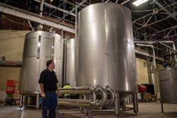 Jason Barrett stands next to one of Black Button Distilling's massive vessels at the University Ave. production facility. - PHOTO BY JACOB WALSH