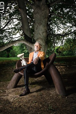Wendell Castle, photographed outside his Scottsville studio in 2016, seated on a chair of his own creation and holding a scale model of another sculpture. - FILE PHOTO