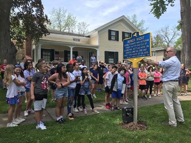 Perinton Town Historian Bill Poray presents a new historic marker before an audience of schoolchildren on May 20, 2022. The marker replaced one that had commemorated the "first white child" born in what is now the village of Fairport.