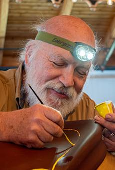 Wearing a head lamp, Gaylon Arnold leans in to paint the gold trim on a saddle on a carousel horse.